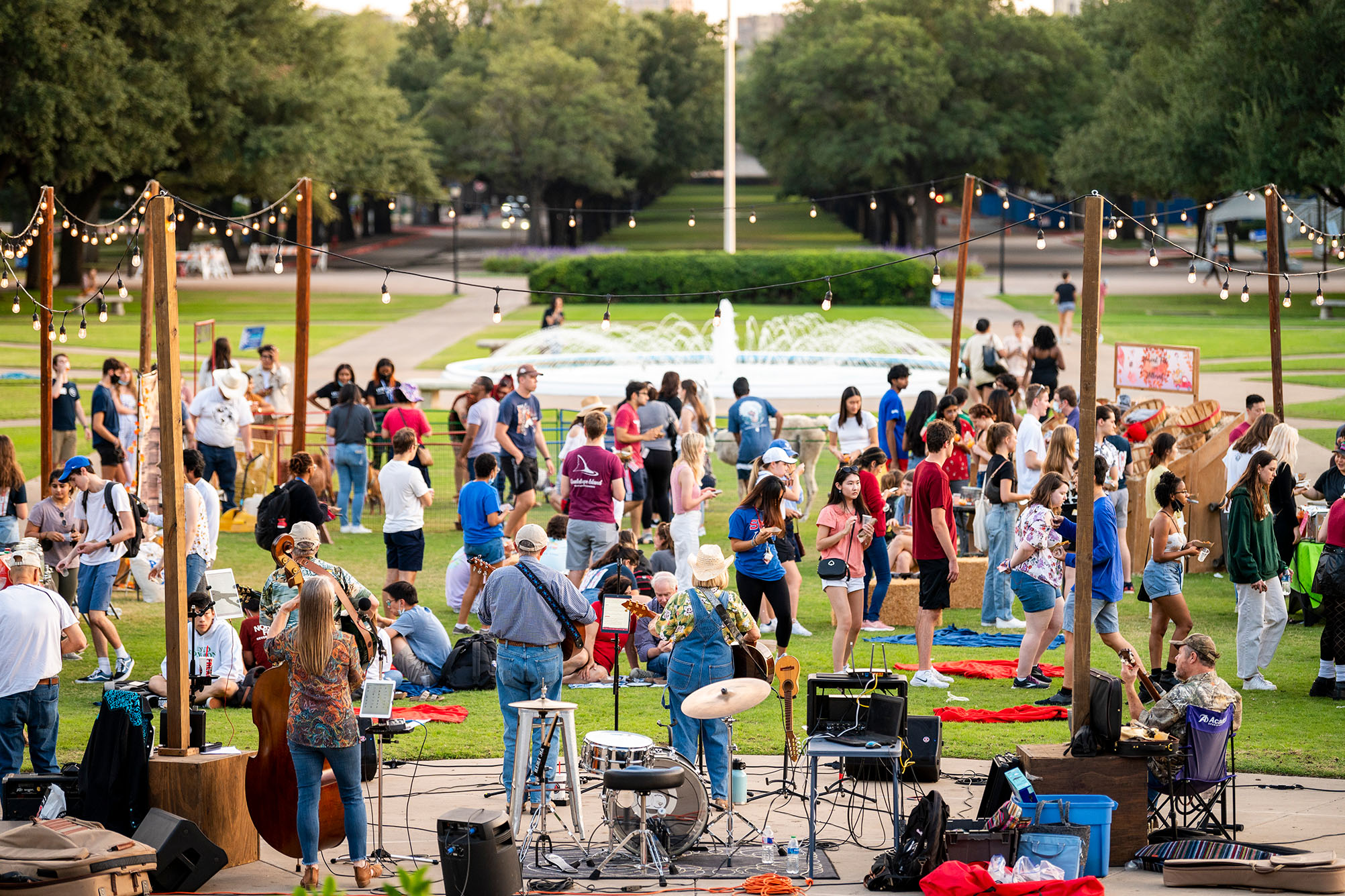 large event outside on grass in front of fountain with people talking and smiling, band playing music on stage